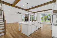 An additional view of the living space from the kitchen accenting the gorgeous white oak flooring, stained wooden beams on the ceiling and cabinetry.