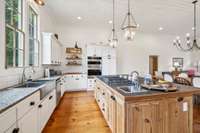 The kitchen is adorned with a white tile backsplash, white cabinets, a double basin sink, an additional utility sink in the tiled island, double ovens, and charming wood shelving that combines aesthetic and function. 5901 Givens Rd Lascassas, TN