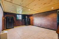 Basement has solid poured concrete walls, security door for window and radiant floor heat. Both safes and the tv cabinet stand remain.