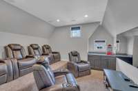 Theater room features tiered seating, dry bar, built-in speakers, black out shades, and recessed lighting.