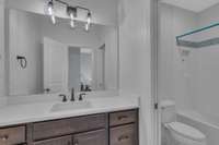 Ensuite bathroom to bedroom 3 features a spacious vanity with white quartz countertops, rectangular sink, storage galore, and a large mirror. Gleaming tile shower/tub combination with sparkling white ceramic and accent tile.