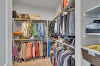 "Her" primary suite closet is L-shaped with plenty of wooden shelving and double hanging rods. Sizable space for every season!