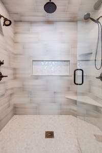 Newly tiled walk-in shower with dual shower heads, rain shower and recessed shampoo niche.