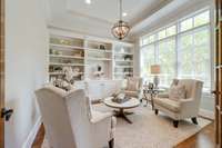 Just through the French doors is an inviting formal living room/study with built in shelving and a tray ceiling.  The wall of windows including transoms makes this space light & bright.