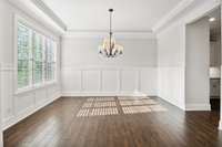 The Dining Room features hardwood flooring, tray ceiling, and an oil rubbed bronze shaded chandelier. Architectural elements include a large triple window and judge’s paneling.