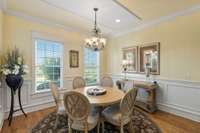 Elegant dining area with large windows providing abundant natural light, a stylish chandelier, classic wainscoting and beautiful hardwood floors.