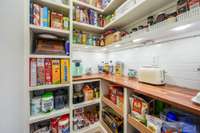 Custom pantry with butcher block prep space, backsplash, and built ins.