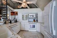 Inside the Barndominium, the kitchen features ceramic tile counters, ceiling fan and spiral stairs to upper loft bedroom area.