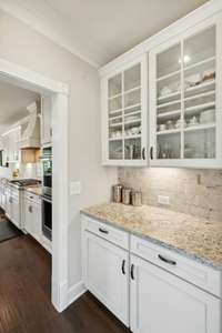 The Butler’s Pantry offers under cabinet lighting, granite countertops, upper cabinets with glass fronts, walk-in pantry, and subway tile backsplash.