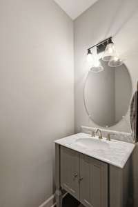 The Main Level Powder Room comes with wood floors, marble topped furniture style vanity with storage, and an oval mirror.