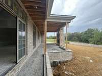 Covered outdoor living featuring a 42" wood-burning, plus an adjoining grilling porch and grade level patio that looks out onto a private backyard with a row of mature trees *this home is under construction. Photo taken: 9/14/24