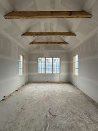 Main Level Primary Bedroom featuring a 15' vaulted Ceiling with stained beam detail.  Plus exterior door to step out into the outdoor living oasis. *this home is under construction.  Photo taken: 9/14/24