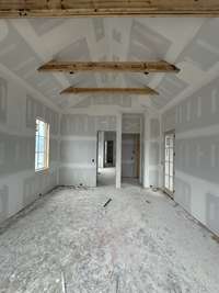 Main Level Primary Bedroom featuring a 15' vaulted Ceiling with stained beam detail.  Plus exterior door to step out into the outdoor living oasis. *this home is under construction.  Photo taken: 9/14/24