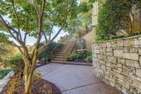 A walkway to the front steps where a beautifully landscaped path leads to a charming garden fountain and elegant stack stone wall
