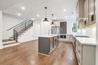 View of Kitchen island with sink and dishwasher and iron stairwell railing.