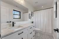 The guest ensuite bathroom upstairs is a thoughtfully designed space that offers both luxury and functionality. It features elegant tile flooring and stone countertops, consistent with the high-quality finishes found throughout the home.