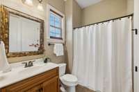 The Main Level Guest Bath has tile flooring, vanity with cabinet storage, and a shower/tub combo. A framed mirror completes the space.