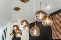 Kitchen island pendants with gold-glazed globes provide a touch of glam against the matte black cabinets and warm wood range hood