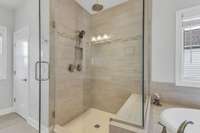 Walk-in shower with seated bench and seamless shower door/surround.