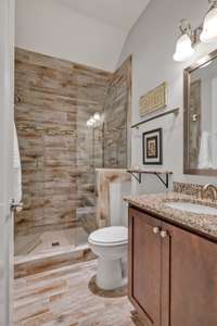 Main level guest bath has walk-in shower, elevated height vanity with granite countertop. 6x24 wood-look tile on floor and shower surround along with a seamless glass door.