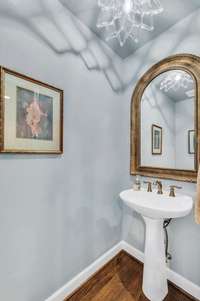 A powder room is just off the kitchen with hardwood floors and custom mirror.