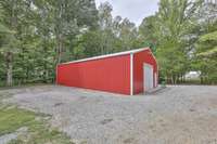 The left side of the barn features a gravel parking pad to keep your items out of view if needed. Notice the tree line behind the 30x50 detached building. The barn is within walking distance of the home.