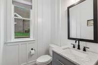 The half bath has heavy wainscoting, a furniture style vanity with marble top, black matte fixtures and framed mirror.