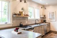 The updated kitchen features a gas range, open shelving, and copious amounts of natural light.