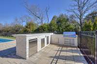 Outdoor kitchen with gas grill, sink, fridge, trash, and storage.