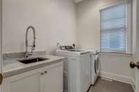 The laundry room includes an appropriately placed utility sink surrounded by marble with additional cabinet storage. The lovely and utilitarian wood tile flooring is quite the suitable choice for this space.