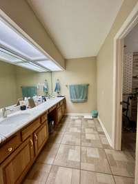 Primary Bath has extra long double vanities with marble tops and space for chair; Tile floor and ample lighting; Wheelchair Accessible doors leading to the wheelchair accessible open shower