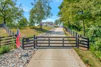 Gated entrance with a long, concrete private driveway leading to a beautiful estate, surrounded by lush greenery and serene landscapes.