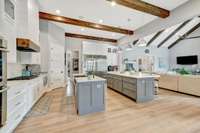 Modern kitchen with dual islands, exposed beams, stainless steel appliances, large walk in corner pantry, white cabinetry, and open layout connecting to the living area.