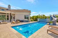 Expansive outdoor area with a sparkling pool, water slide, fire pit, and lounge chairs, surrounded by serene countryside views.