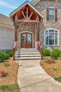 Charming front entrance with arched double doors, stone facade, and rustic wooden beams under a covered porch