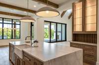 Oversized waterfall peninsula with a large apron sink and customized pantry cabinet with glass doors and slats makes for a chic and functional choice.