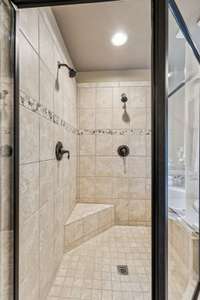 The walk-in shower features dual shower heads, a corner seat and glass door.