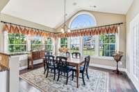 The spacious breakfast room features walls of windows and an arched window, Access to the deck is to the right.