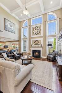 The 2-story great room features a coffered ceiling, floor-to-ceiling windows, hardwood flooring and a fireplace