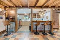 Between the main living area and the kitchen is a peninsula countertop with bar seating, inviting conversation while meals are prepared. Unique details like corrugated metal trim and roped chandelier lighting add character.