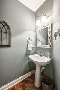 Main level powder room is located in the front entry~Hardwood floors, pedestal sink, elevated elongated toilet and decorative mirror.