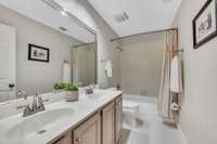 Second floor full bathroom with double vanity, plate glass mirror, tile shower and brushed chrome fixtures.