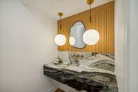 1/2 bath located off the living space features this custom stone vanity, reeding wood, and designer lighting.