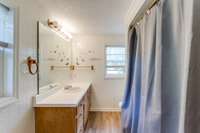 The roomy bathroom has a large vanity, laminate flooring and shower/tub combo.