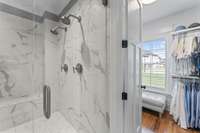 Large tiled shower has double shower heads and a large bench.