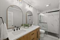 The lower level Guest Bathroom: Natural Oak & Quartz Double Sink Vanity, Delta Black fixtures, shower head with handheld, Custom tilework in shower & niche, vanity is equipped with power source in pull out.