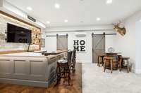 Designed for entertaining, this stunning custom bar features quartzite countertops, Above the bar a large TV is perfectly positioned making it ideal for enjoying sports events. The barn doors stylishly hide additional storage space.