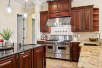 This stunning chef's kitchen features custom cherry cabinets. At the center is a powerful stainless steel gas stove with double ovens, perfect for preparing meals. Granite countertops compliment the design. Walk in pantry located to the left.