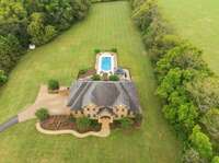 This captivating aerial view highlights the beauty and elegance of the home and its surroundings. From above you can admire rows of mature trees offering privacy. If you look closely you'll spot a quaint chicken coop tucked away on the left.