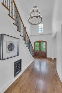 The grand foyer features a multiple tier chandelier, iron staircase, custom iron vent and hardwood floors.